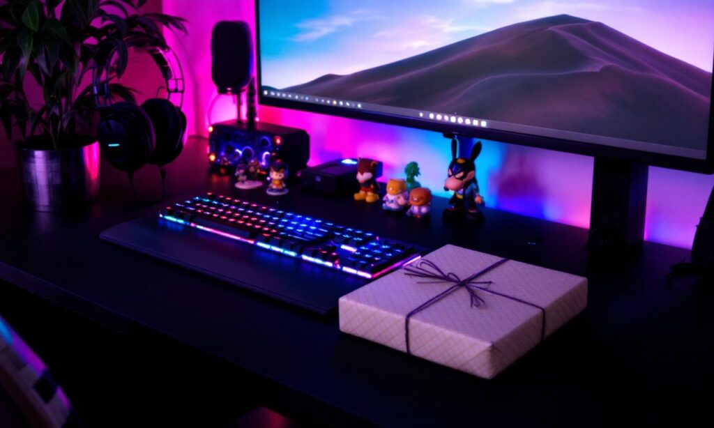 A vibrant gaming setup with accessories like a headset, LED keyboard, collectible figurines, and a gift-wrapped box on the desk.